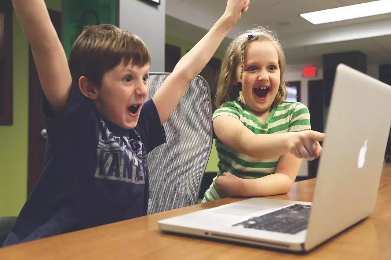 Junge und Mädchen sitzen vor dem Laptop und freuen sich