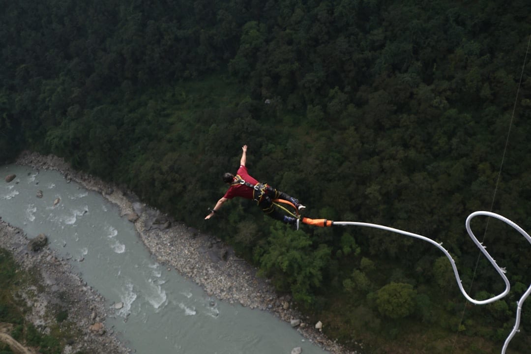 A man is parasailing over a river in the mountains